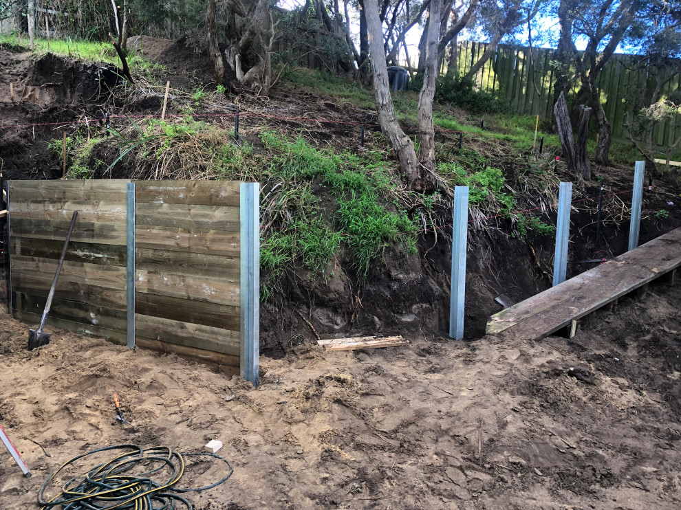Expansive contemporary backyard shaded formal garden in Melbourne with a retaining wall and a wood fence for summer.