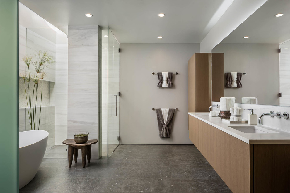This is an example of a contemporary master bathroom in San Francisco with flat-panel cabinets, medium wood cabinets, a freestanding tub, a curbless shower, white tile, white walls, an undermount sink, grey floor, a hinged shower door and white benchtops.