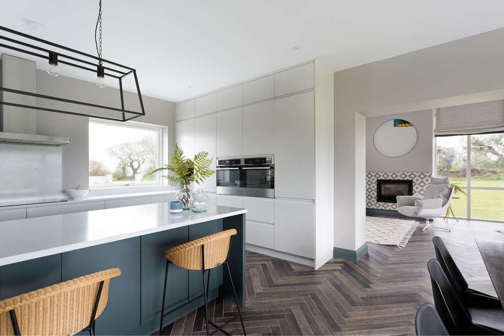 This is an example of a large contemporary l-shaped eat-in kitchen in Cork with an undermount sink, flat-panel cabinets, grey cabinets, quartzite benchtops, white splashback, glass sheet splashback, stainless steel appliances, ceramic floors, with island, brown floor and white benchtop.