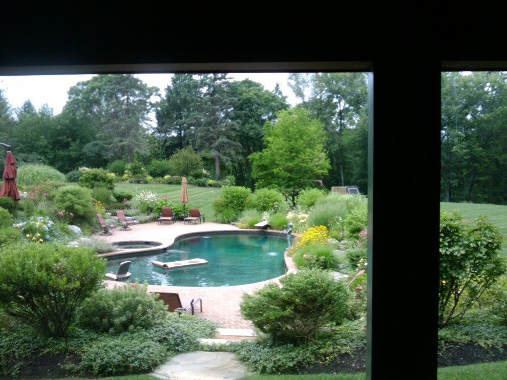 This is an example of a mid-sized country backyard custom-shaped natural pool in Louisville with a water feature and brick pavers.
