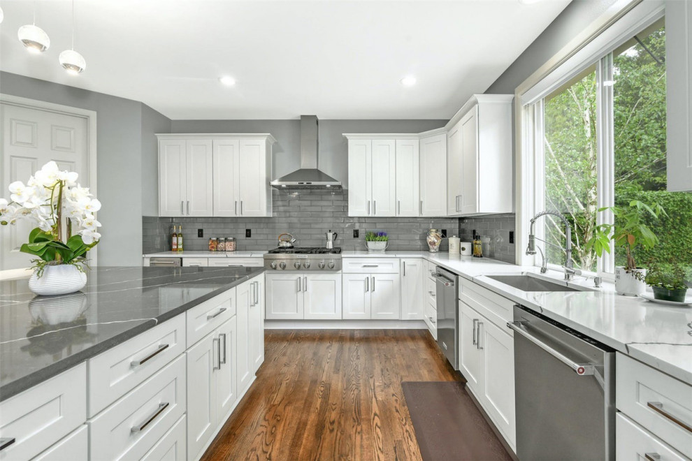 Photo of a large traditional u-shaped kitchen/diner in Seattle with a submerged sink, shaker cabinets, white cabinets, marble worktops, grey splashback, glass tiled splashback, stainless steel appliances, medium hardwood flooring, an island, brown floors and white worktops.