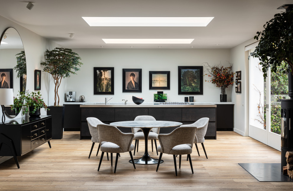 Foto di una sala da pranzo aperta verso la cucina contemporanea con pareti bianche, parquet chiaro, stufa a legna e pavimento beige