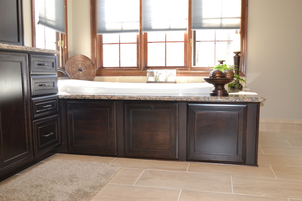 This is an example of a large transitional master bathroom in Columbus with an undermount sink, recessed-panel cabinets, dark wood cabinets, granite benchtops, a drop-in tub, a double shower, a one-piece toilet, black tile, porcelain tile, beige walls and porcelain floors.