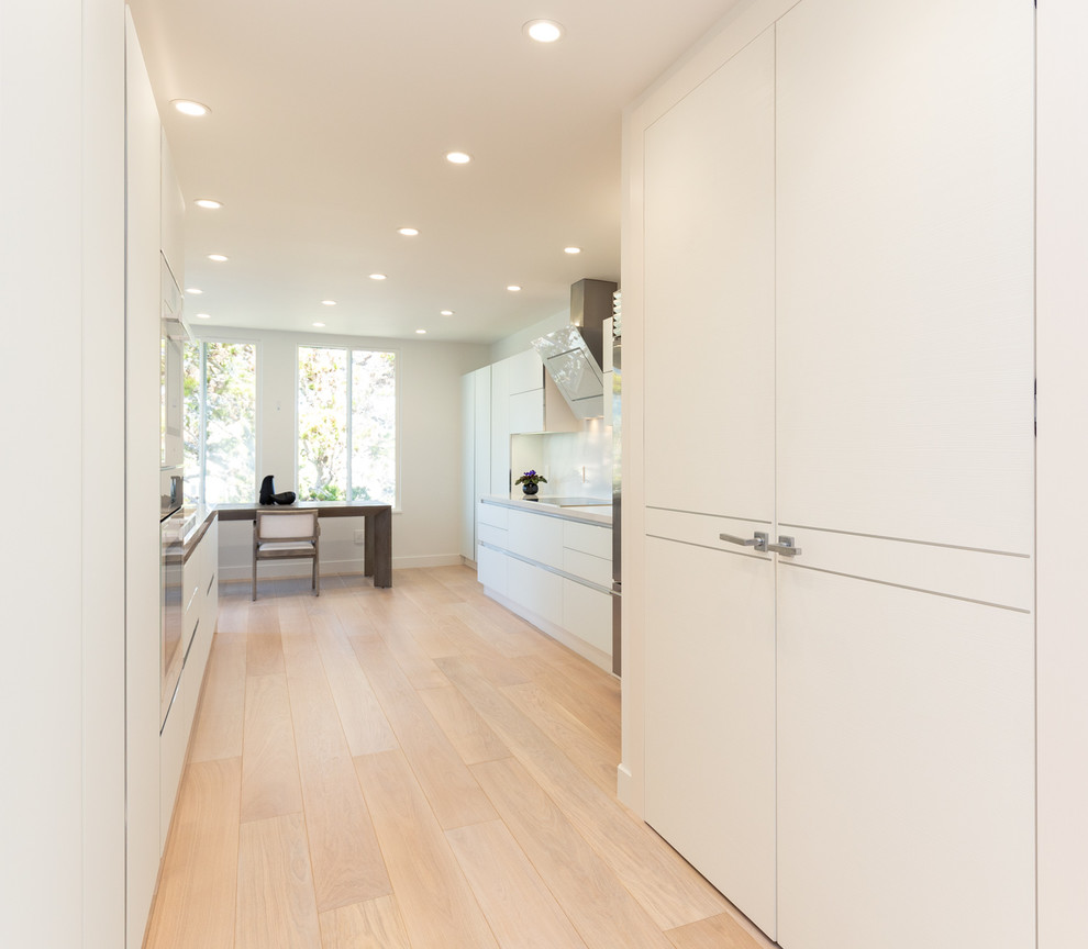 Design ideas for a mid-sized modern galley eat-in kitchen in San Francisco with an undermount sink, flat-panel cabinets, white cabinets, quartz benchtops, white splashback, white appliances, light hardwood floors, no island, brown floor and white benchtop.