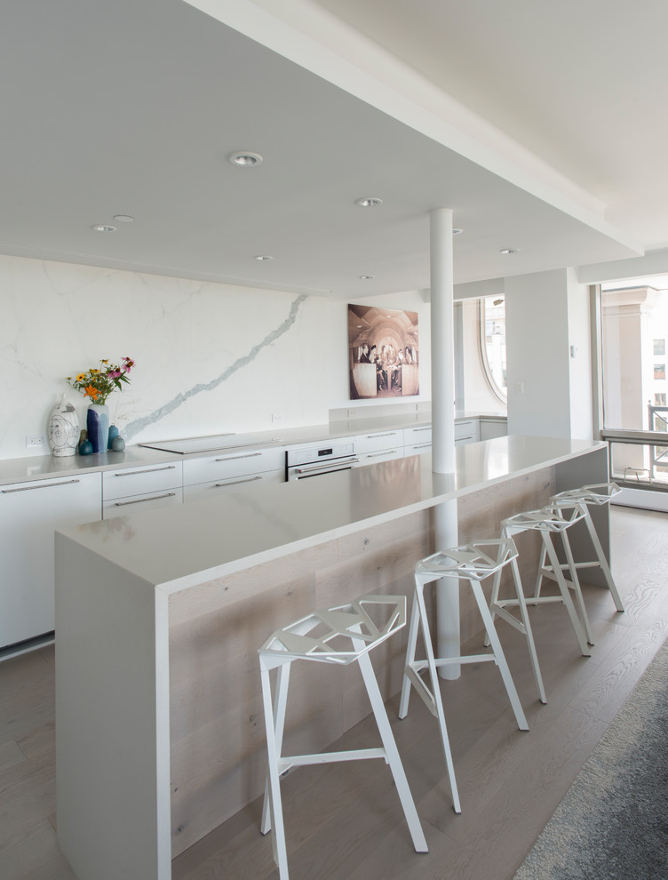 Mid-sized contemporary galley eat-in kitchen in DC Metro with flat-panel cabinets, white cabinets, quartz benchtops, white splashback, porcelain splashback, panelled appliances, light hardwood floors, with island and beige floor.