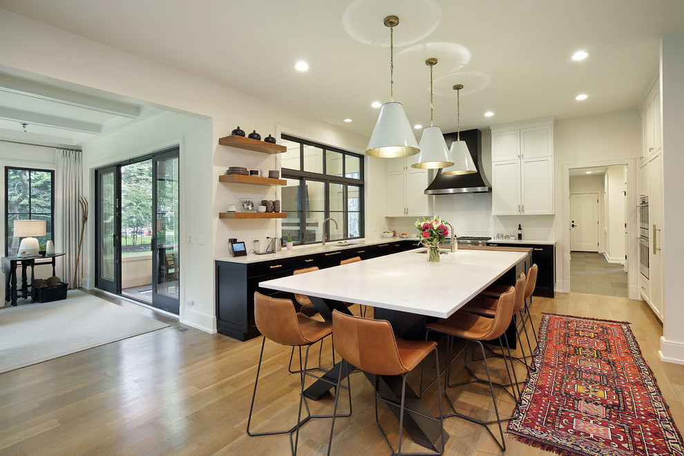 Photo of a large transitional l-shaped eat-in kitchen in Chicago with an undermount sink, recessed-panel cabinets, black cabinets, quartzite benchtops, white splashback, ceramic splashback, stainless steel appliances, medium hardwood floors, with island, brown floor and white benchtop.