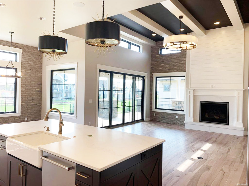 Design ideas for a country l-shaped open plan kitchen in Denver with a farmhouse sink, shaker cabinets, white cabinets, quartz benchtops, white splashback, ceramic splashback, stainless steel appliances, light hardwood floors, with island, beige floor and white benchtop.