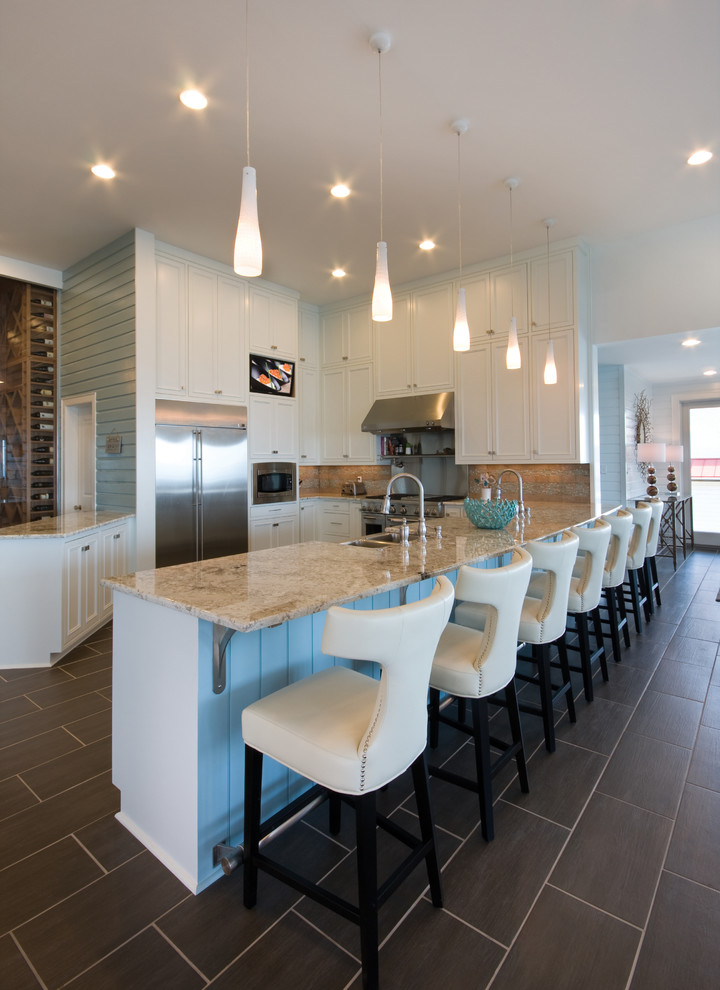 Photo of a beach style u-shaped open plan kitchen in New Orleans with shaker cabinets, white cabinets, beige splashback, stainless steel appliances, slate floors, with island, a farmhouse sink, granite benchtops, ceramic splashback and grey floor.