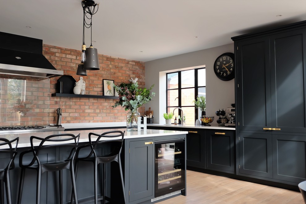This is an example of a transitional l-shaped kitchen in Other with shaker cabinets, black cabinets, brick splashback, light hardwood floors, with island, beige floor and white benchtop.