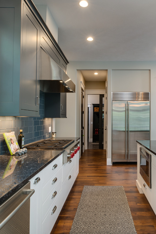 Inspiration for a large transitional single-wall medium tone wood floor open concept kitchen remodel with an undermount sink, shaker cabinets, gray cabinets, granite countertops, gray backsplash, ceramic backsplash, stainless steel appliances and an island