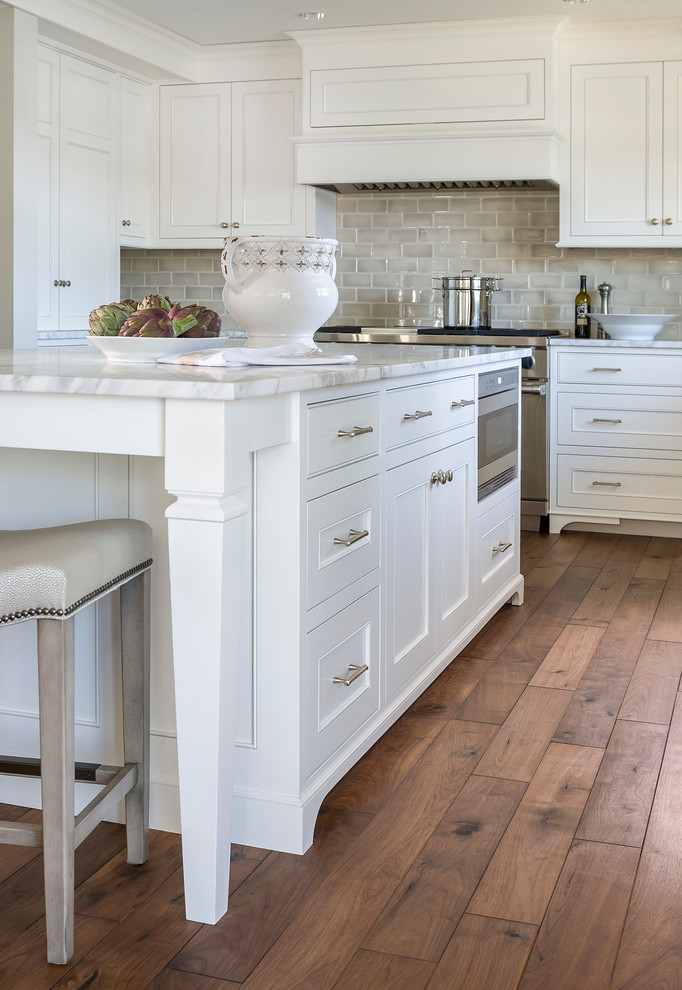 Inspiration for a mid-sized traditional l-shaped eat-in kitchen in Minneapolis with an undermount sink, recessed-panel cabinets, white cabinets, marble benchtops, grey splashback, ceramic splashback, dark hardwood floors, with island and stainless steel appliances.