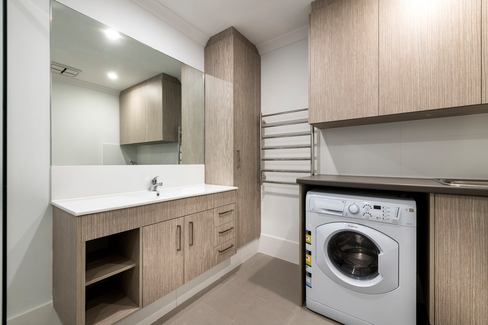 This is an example of a small modern utility room in Perth with recessed-panel cabinets, light wood cabinets, laminate benchtops, white walls, porcelain floors, a stacked washer and dryer, brown floor and an integrated sink.