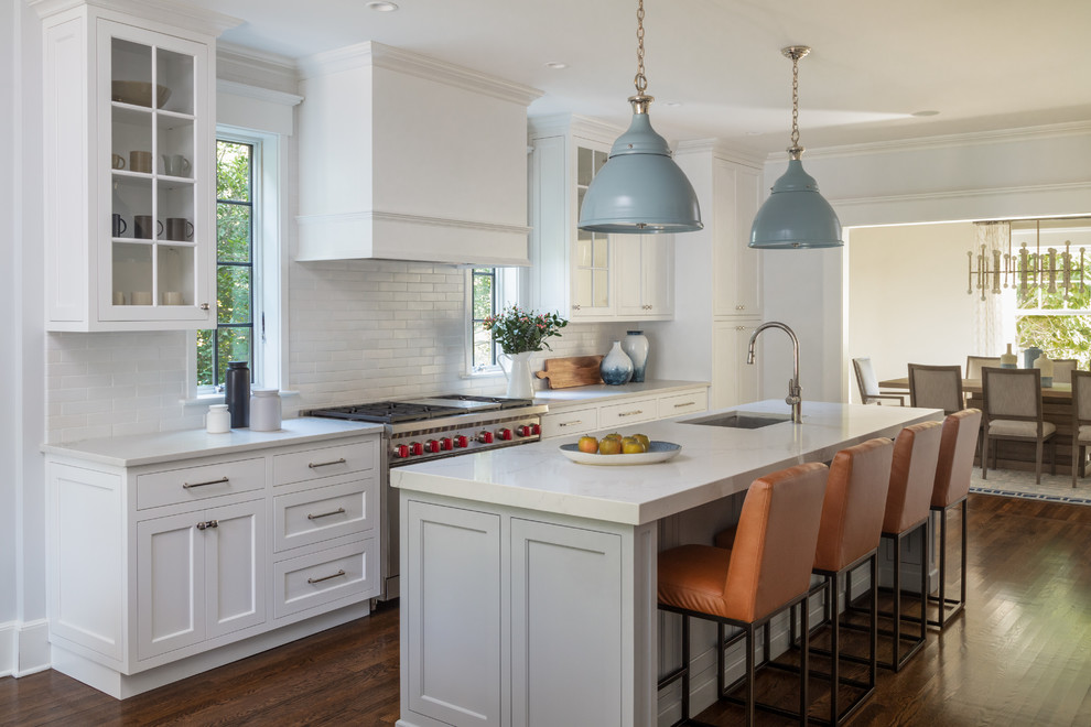 Transitional galley kitchen in New York with an undermount sink, shaker cabinets, white cabinets, white splashback, stainless steel appliances, dark hardwood floors, with island, brown floor and white benchtop.