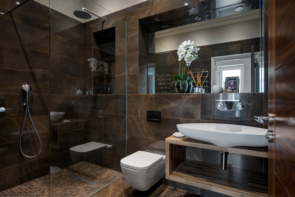 This is an example of a mid-sized contemporary 3/4 bathroom in Surrey with brown tile, ceramic tile, ceramic floors, brown floor, an open shower, a wall-mount toilet, a vessel sink, open cabinets, a curbless shower and brown benchtops.