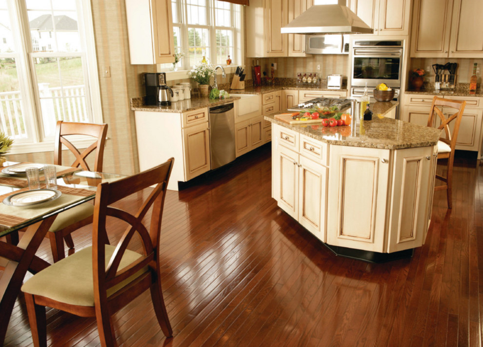 Example of a large transitional u-shaped medium tone wood floor and brown floor eat-in kitchen design with a farmhouse sink, beaded inset cabinets, beige cabinets, granite countertops, beige backsplash, ceramic backsplash, stainless steel appliances and an island