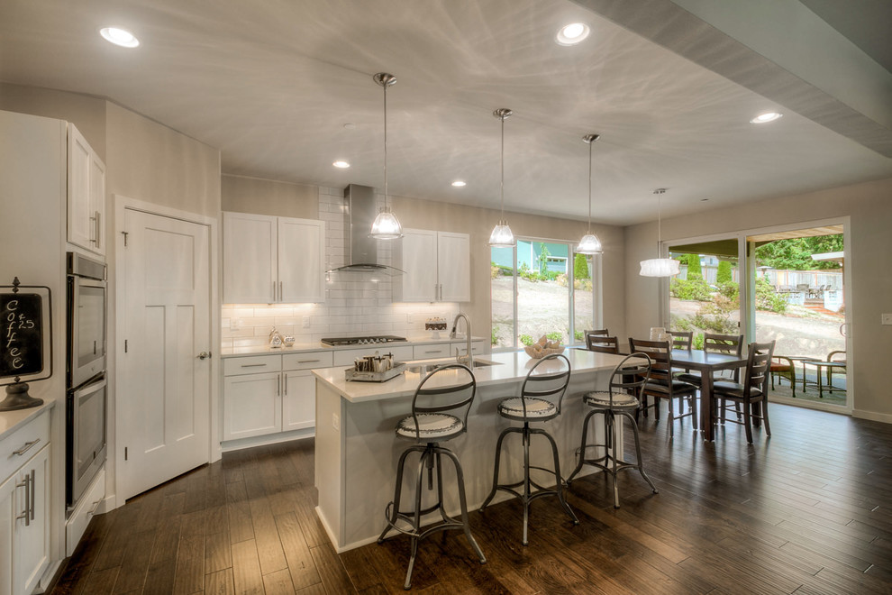 Large contemporary l-shaped eat-in kitchen in Seattle with an undermount sink, shaker cabinets, white cabinets, granite benchtops, white splashback, subway tile splashback, stainless steel appliances, dark hardwood floors and with island.