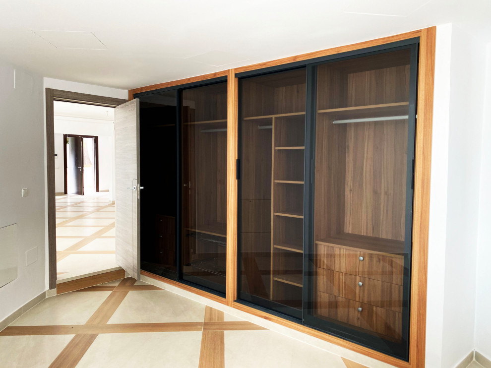 Immagine di una cabina armadio unisex design di medie dimensioni con ante di vetro, ante in legno scuro, pavimento in gres porcellanato, pavimento marrone e soffitto ribassato