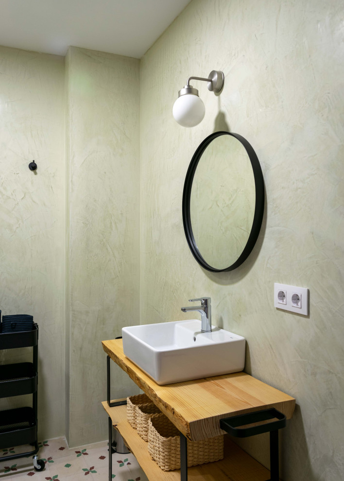 Medelhavsstil inredning av ett litet badrum med dusch, med öppna hyllor, skåp i ljust trä, våtrum, en toalettstol med hel cisternkåpa, gröna väggar, klinkergolv i keramik, ett fristående handfat, träbänkskiva, flerfärgat golv och dusch med skjutdörr