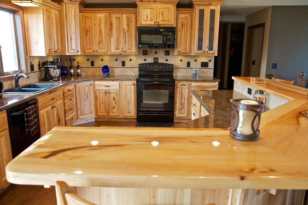 Example of a large l-shaped open concept kitchen design with a drop-in sink, raised-panel cabinets, light wood cabinets, laminate countertops, beige backsplash, stone tile backsplash, black appliances and an island
