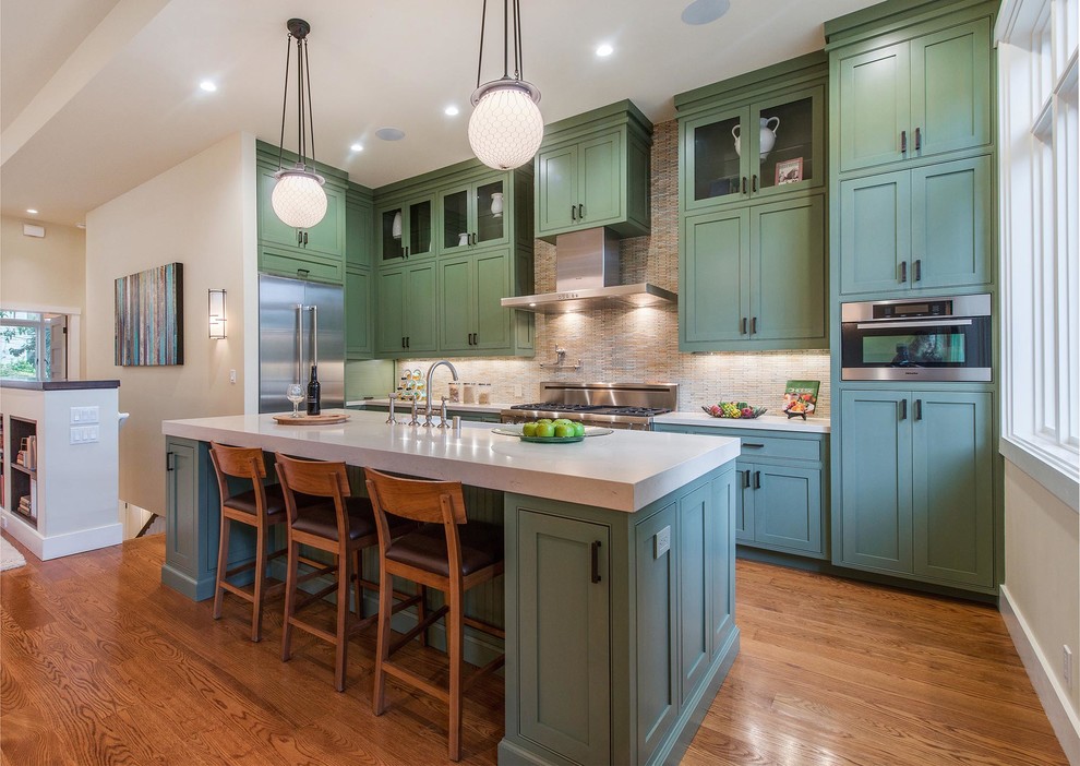 This is an example of a mid-sized transitional l-shaped open plan kitchen in San Francisco with a farmhouse sink, recessed-panel cabinets, green cabinets, quartz benchtops, beige splashback, ceramic splashback, stainless steel appliances, medium hardwood floors and with island.