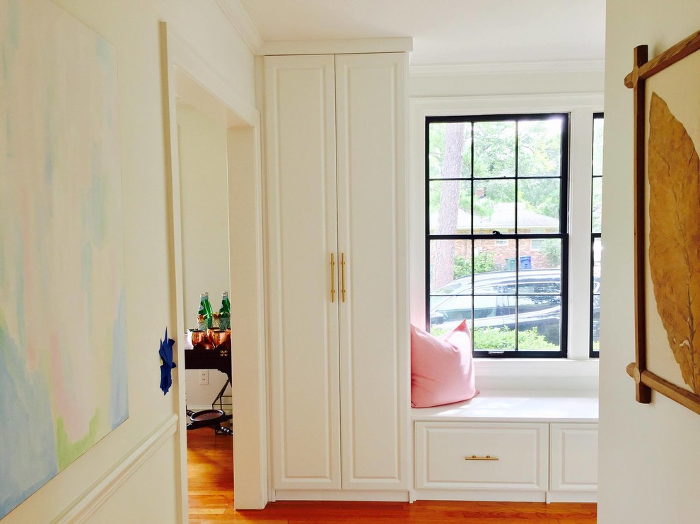 This is an example of a mid-sized shabby-chic style utility room in Other with white cabinets, white walls, medium hardwood floors, a concealed washer and dryer and brown floor.