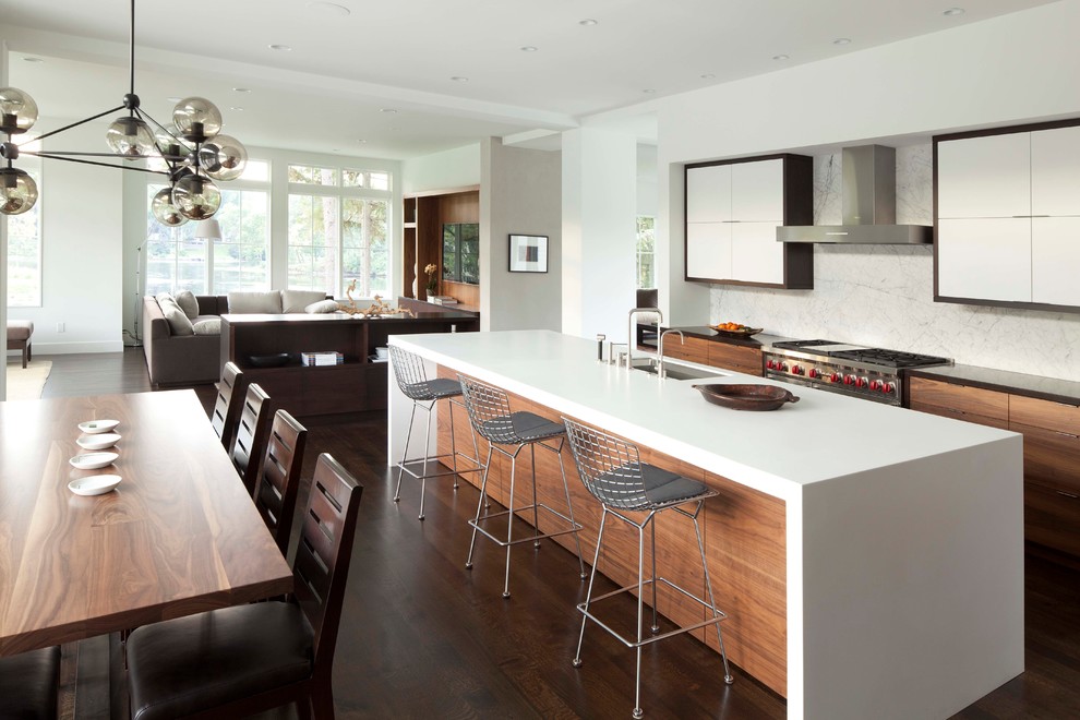 Photo of a contemporary l-shaped open plan kitchen in Minneapolis with an undermount sink, flat-panel cabinets, solid surface benchtops, white splashback, stone slab splashback, stainless steel appliances and white cabinets.