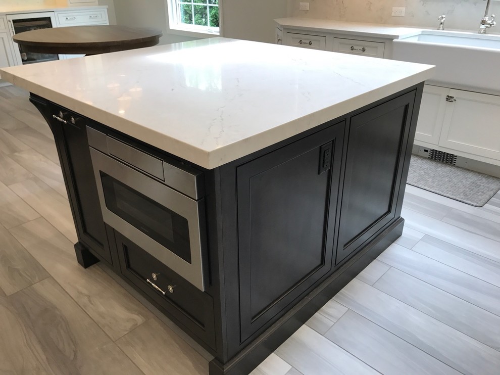Mid-sized transitional u-shaped light wood floor and brown floor open concept kitchen photo with a farmhouse sink, recessed-panel cabinets, white cabinets, marble countertops, white backsplash, marble backsplash, stainless steel appliances and an island