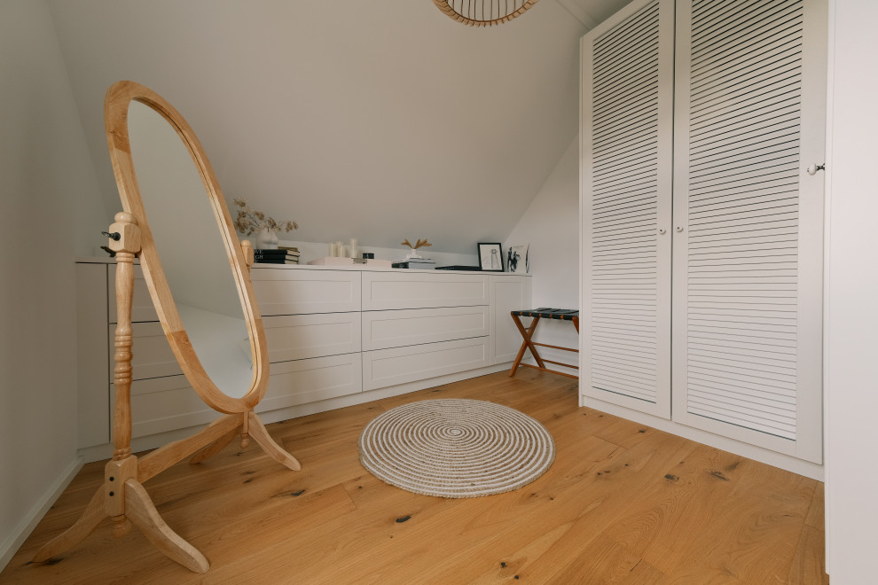 Kleines Nordisches Ankleidezimmer mit Ankleidebereich, Lamellenschränken, weißen Schränken, braunem Holzboden, braunem Boden und Tapetendecke in Berlin