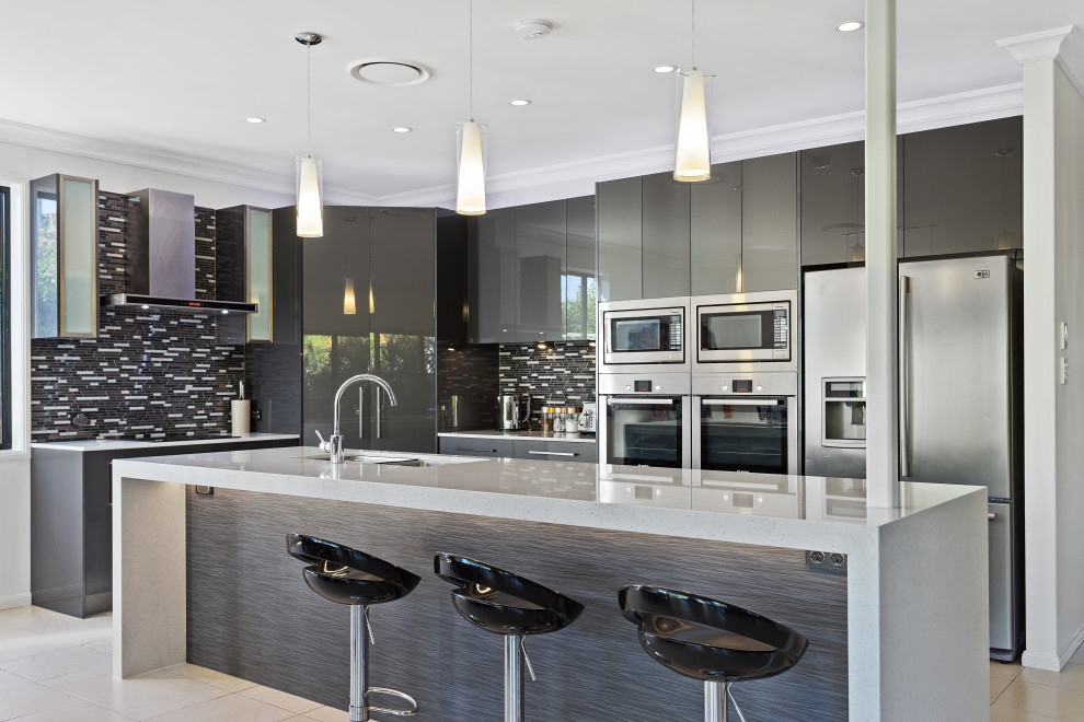 Photo of a large contemporary l-shaped kitchen in Gold Coast - Tweed with an undermount sink, flat-panel cabinets, grey cabinets, grey splashback, matchstick tile splashback, stainless steel appliances, porcelain floors, with island, beige floor and grey benchtop.