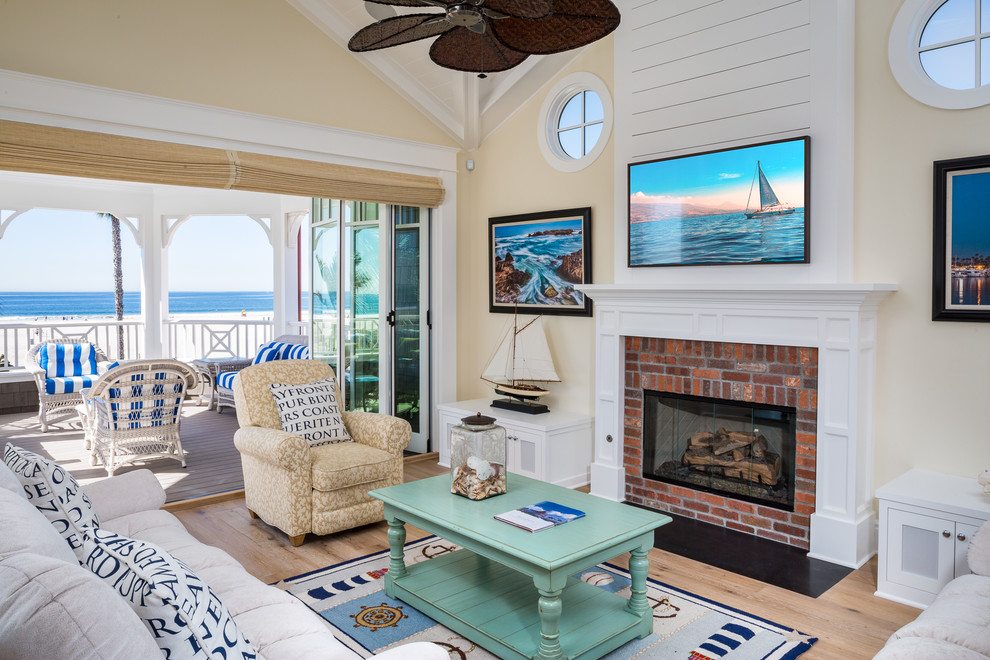 This is an example of a large beach style family room in San Diego with yellow walls, light hardwood floors, a ribbon fireplace, a brick fireplace surround and a wall-mounted tv.