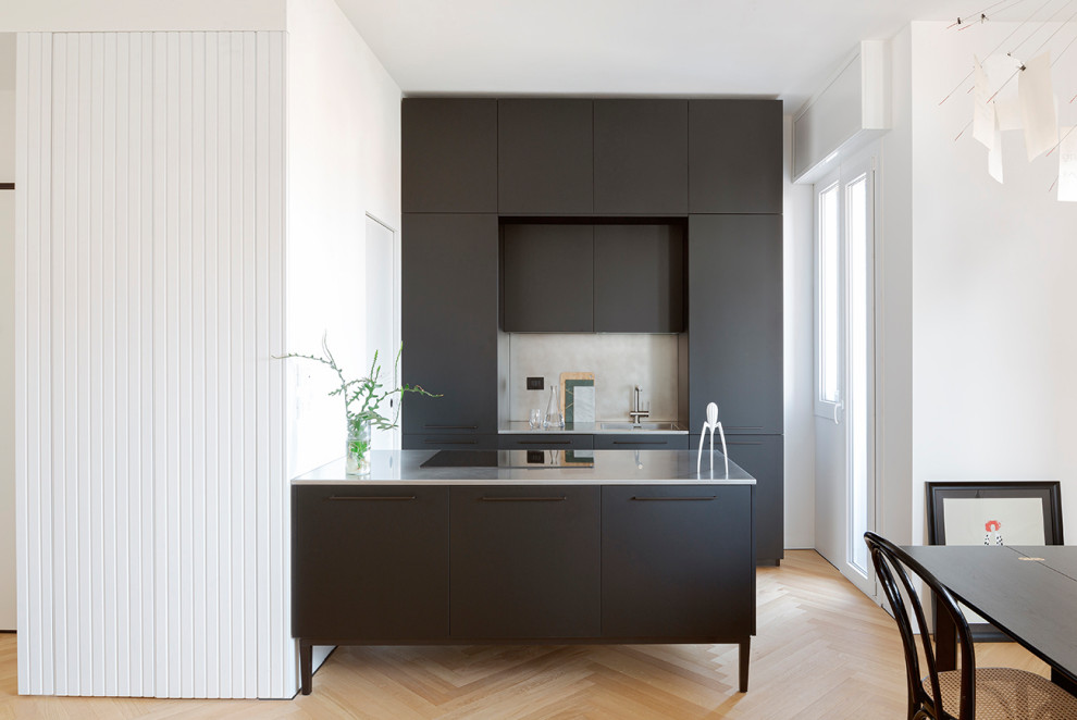 Exempel på ett litet modernt kök, med en integrerad diskho, släta luckor, svarta skåp, bänkskiva i rostfritt stål, rostfria vitvaror, ljust trägolv och en köksö