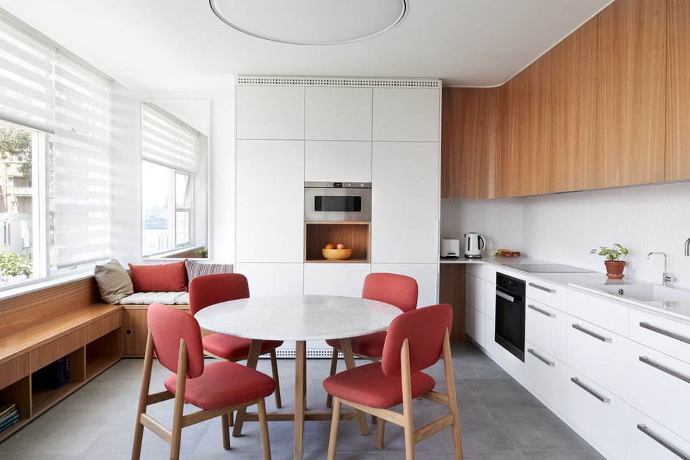 Contemporary l-shaped eat-in kitchen in Sydney with a drop-in sink, flat-panel cabinets, white cabinets, white splashback, black appliances and no island.
