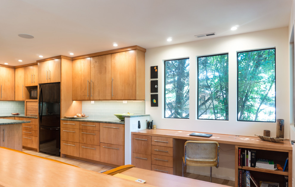 This is an example of a mid-sized contemporary u-shaped open plan kitchen in Boise with an undermount sink, flat-panel cabinets, medium wood cabinets, granite benchtops, green splashback, glass tile splashback, black appliances, light hardwood floors and with island.