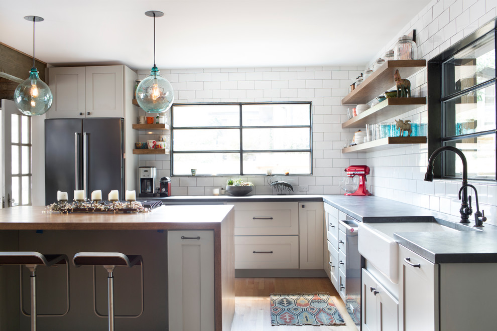 Mid-sized transitional u-shaped light wood floor eat-in kitchen photo with a farmhouse sink, flat-panel cabinets, white cabinets, white backsplash, ceramic backsplash, stainless steel appliances and an island