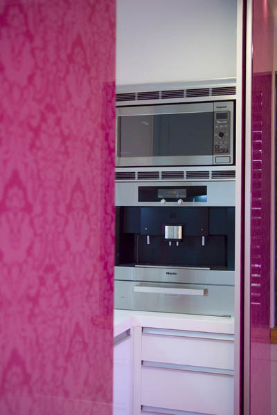 Design ideas for a large modern galley kitchen in Los Angeles with flat-panel cabinets, quartz benchtops, pink splashback, glass sheet splashback, stainless steel appliances, light hardwood floors and with island.