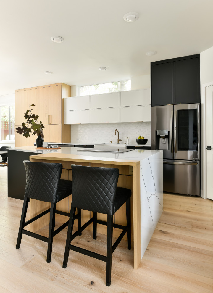 Photo of a large modern single-wall eat-in kitchen in Seattle with a farmhouse sink, shaker cabinets, black cabinets, quartz benchtops, white splashback, porcelain splashback, stainless steel appliances, medium hardwood floors, with island, yellow floor and white benchtop.