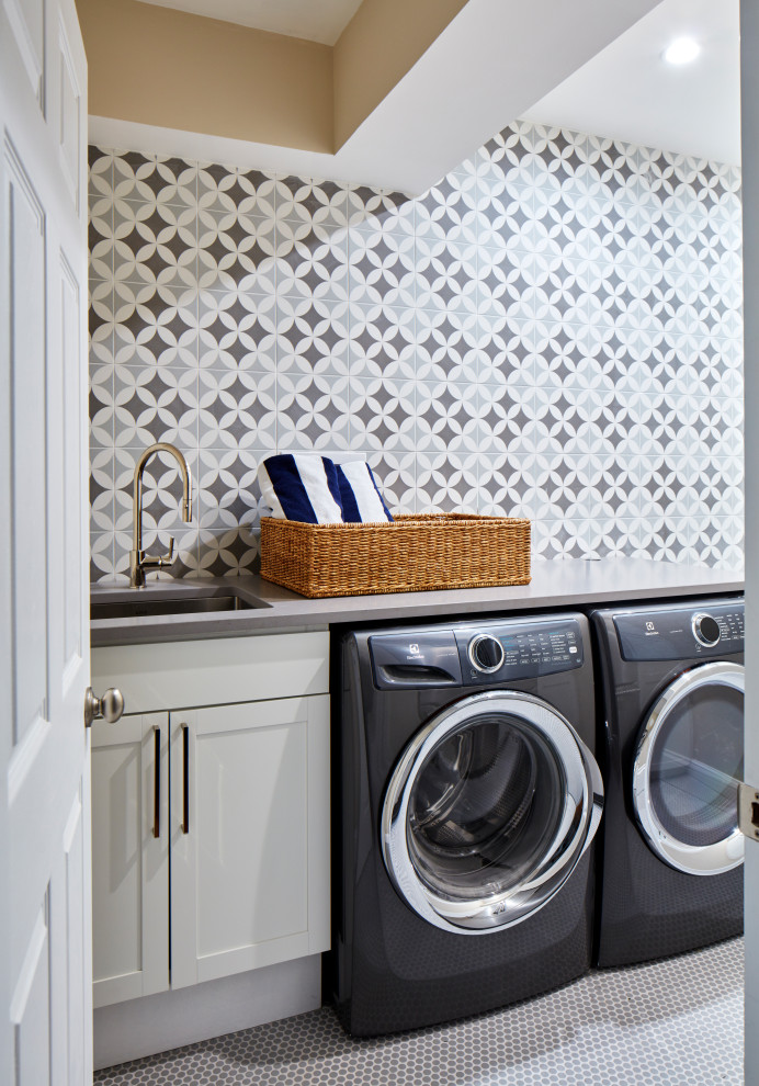 Foto på en mellanstor vintage grå linjär tvättstuga enbart för tvätt, med en undermonterad diskho, skåp i shakerstil, grå skåp, bänkskiva i kvarts, flerfärgad stänkskydd, stänkskydd i porslinskakel, vita väggar, klinkergolv i porslin, en tvättmaskin och torktumlare bredvid varandra och grått golv