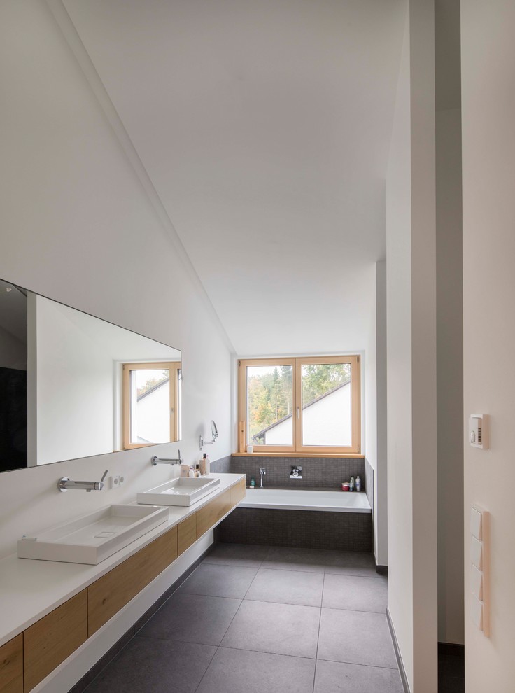 Photo of a mid-sized contemporary 3/4 bathroom in Munich with flat-panel cabinets, light wood cabinets, a drop-in tub, gray tile, mosaic tile, white walls, cement tiles, a vessel sink, grey floor and white benchtops.