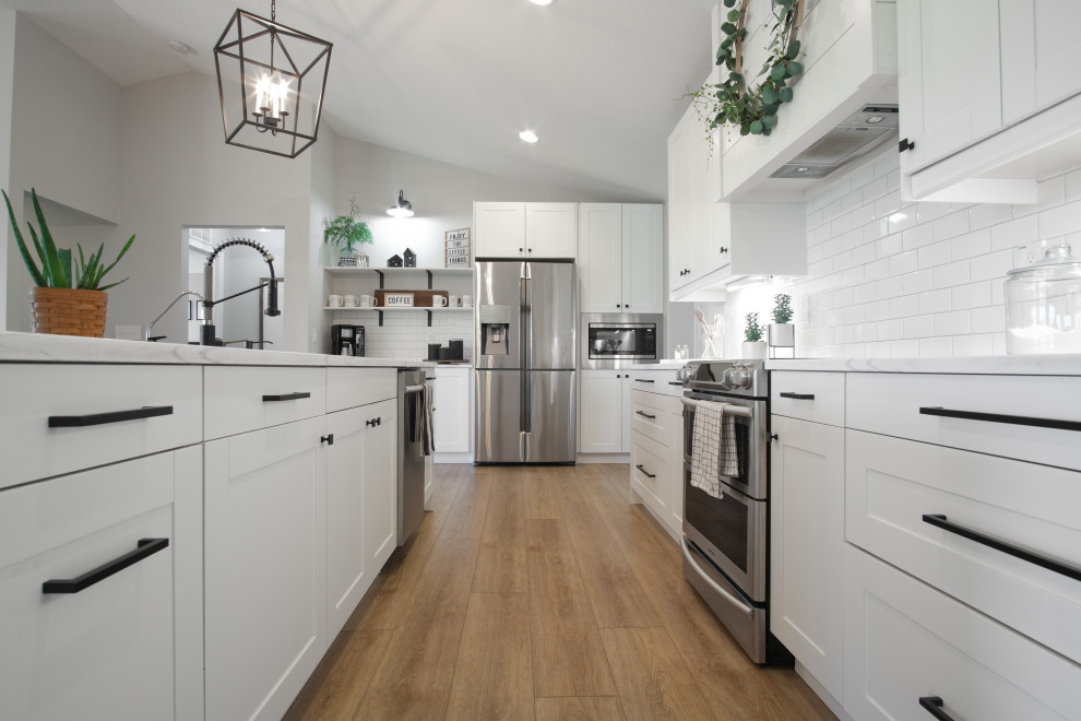 Design ideas for a mid-sized country l-shaped open plan kitchen in Columbus with a drop-in sink, beaded inset cabinets, white cabinets, marble benchtops, white splashback, ceramic splashback, stainless steel appliances, vinyl floors, brown floor, white benchtop, vaulted and with island.