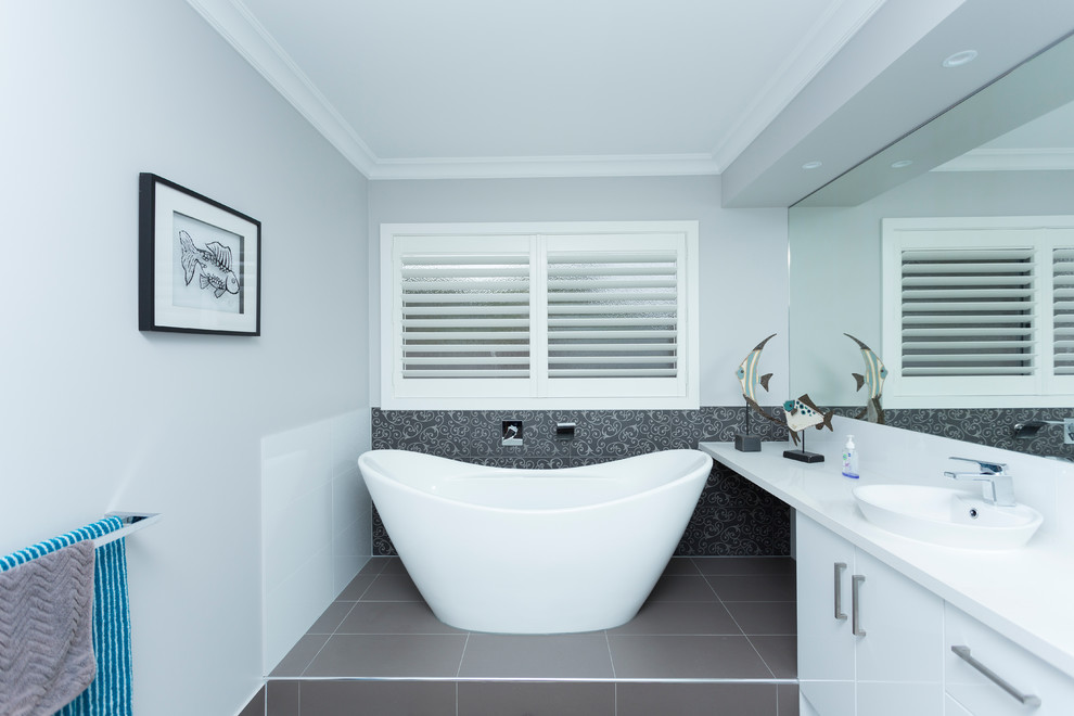 Mid-sized transitional 3/4 bathroom in Melbourne with flat-panel cabinets, white cabinets, a freestanding tub, porcelain tile, grey walls, ceramic floors, grey floor, gray tile, a vessel sink, engineered quartz benchtops and white benchtops.
