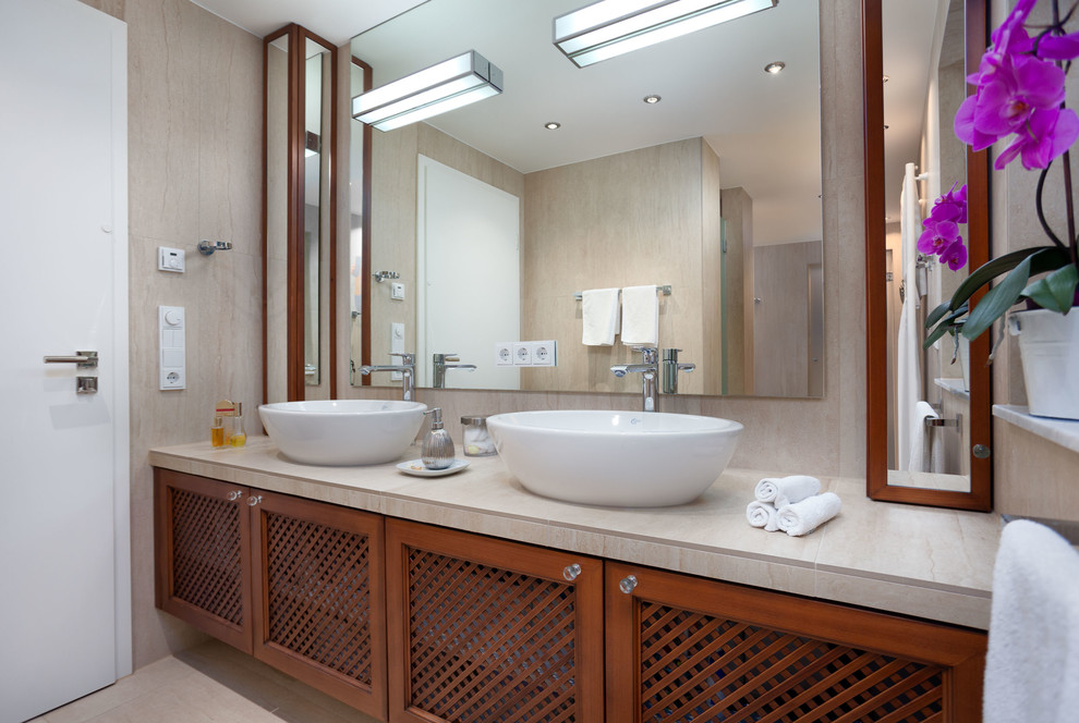 Großes Modernes Duschbad mit profilierten Schrankfronten, hellbraunen Holzschränken, Einbaubadewanne, Wandtoilette mit Spülkasten, beigen Fliesen, Steinfliesen, beiger Wandfarbe, Porzellan-Bodenfliesen, Aufsatzwaschbecken, gefliestem Waschtisch, beigem Boden, Schiebetür-Duschabtrennung, Duschnische und beiger Waschtischplatte in München