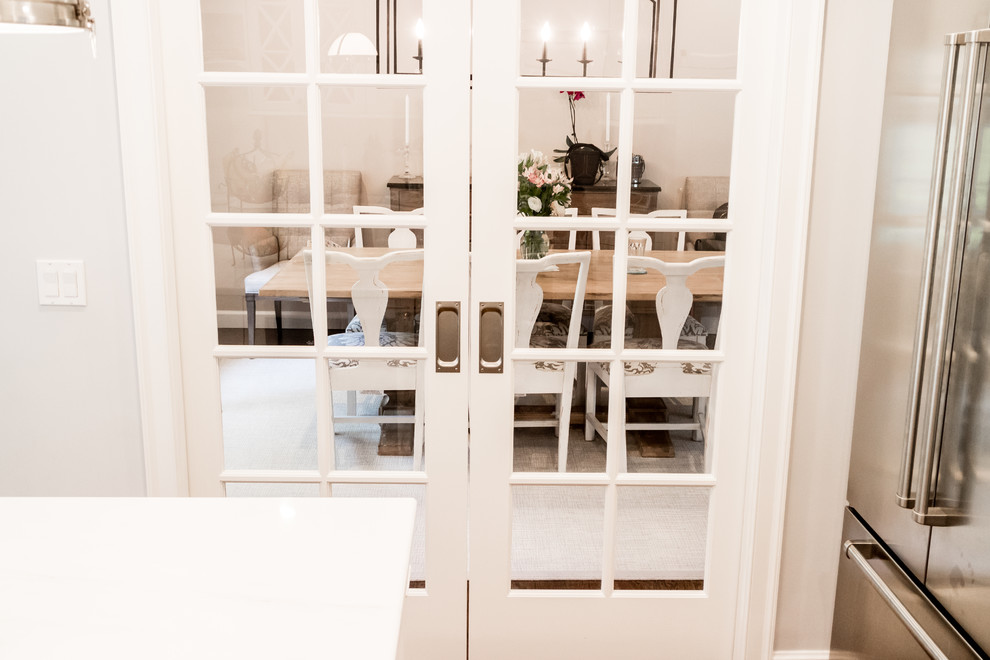 Example of a mid-sized transitional dark wood floor and brown floor enclosed kitchen design in New York with a farmhouse sink, recessed-panel cabinets, white cabinets, quartzite countertops, white backsplash, subway tile backsplash, stainless steel appliances and an island