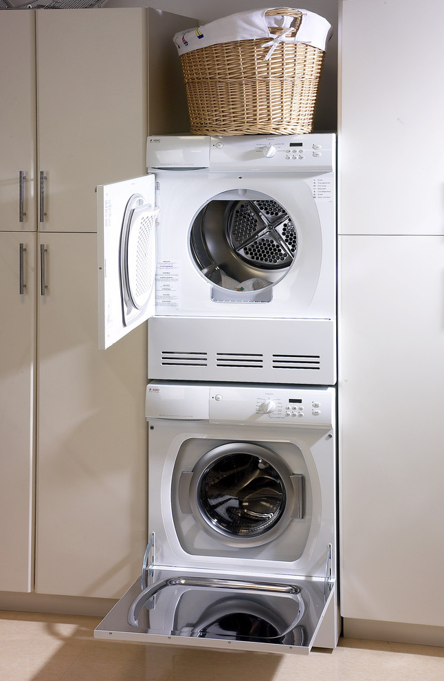 This is an example of a mid-sized modern single-wall dedicated laundry room in Boston with flat-panel cabinets, white cabinets, white walls, ceramic floors, a stacked washer and dryer and beige floor.