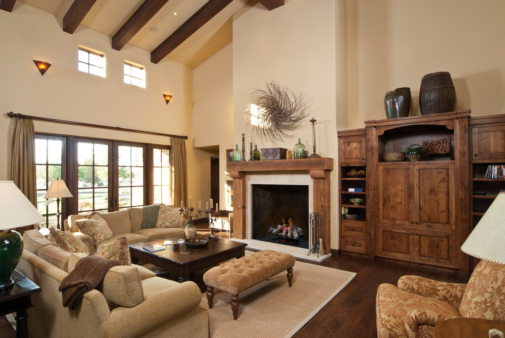 Photo of a large mediterranean open concept family room in Boise with beige walls, dark hardwood floors, a standard fireplace, a wood fireplace surround, brown floor and a concealed tv.