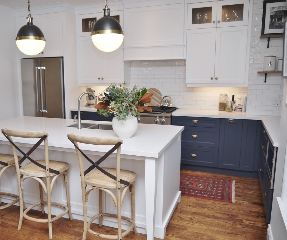 Inspiration for a mid-sized transitional l-shaped medium tone wood floor and brown floor eat-in kitchen remodel in Toronto with an undermount sink, shaker cabinets, blue cabinets, quartz countertops, white backsplash, subway tile backsplash, stainless steel appliances, an island and white countertops