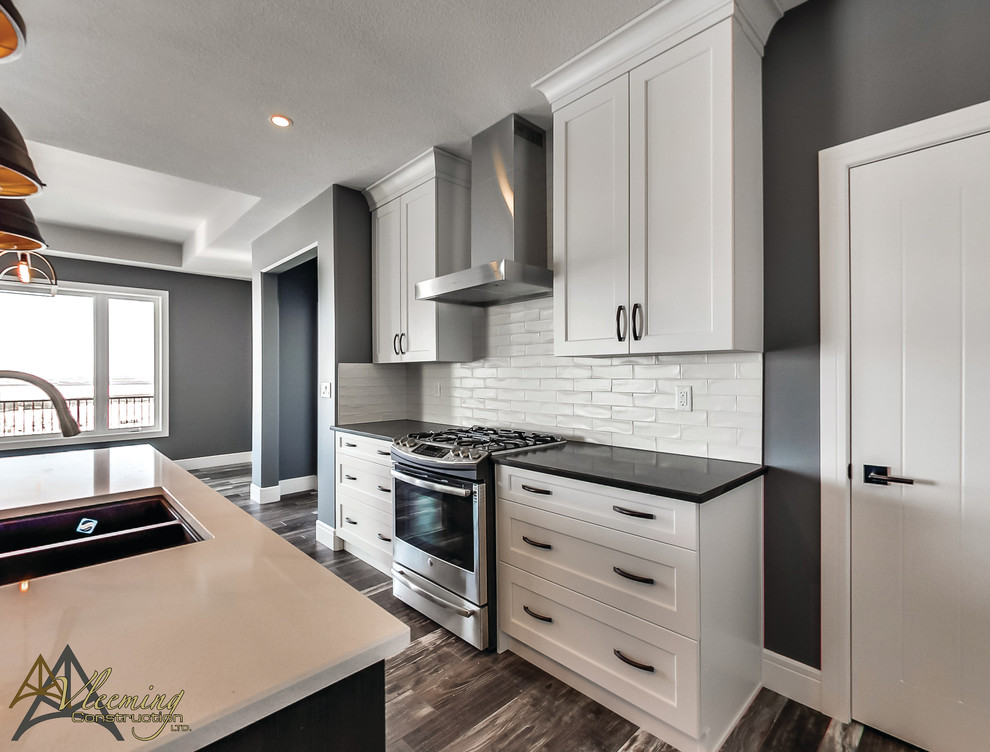 Mid-sized modern l-shaped eat-in kitchen in San Diego with a double-bowl sink, shaker cabinets, white cabinets, solid surface benchtops, white splashback, subway tile splashback, stainless steel appliances, dark hardwood floors and with island.