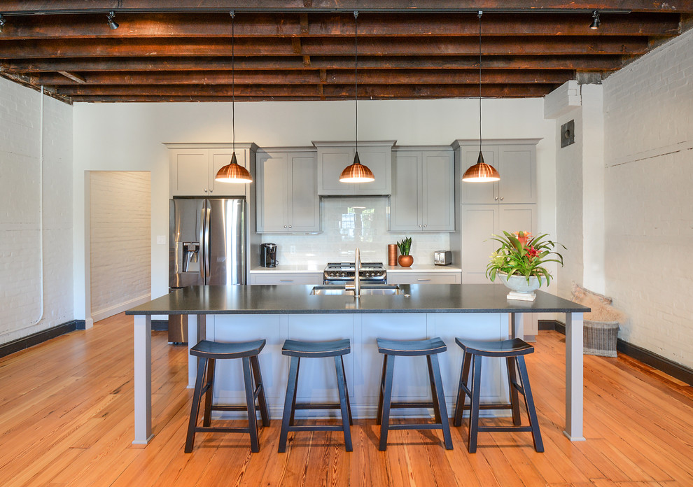 Photo of an industrial galley eat-in kitchen in Charleston with a single-bowl sink, shaker cabinets, grey cabinets, white splashback, glass sheet splashback, stainless steel appliances, medium hardwood floors, with island and brown floor.