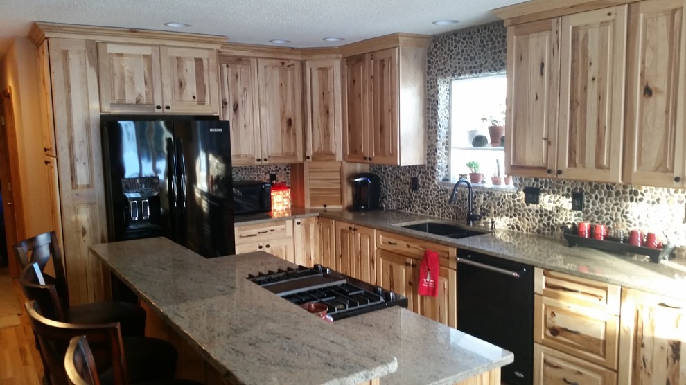 Example of a mid-sized mountain style l-shaped medium tone wood floor and brown floor open concept kitchen design with a double-bowl sink, raised-panel cabinets, light wood cabinets, granite countertops, multicolored backsplash, stone tile backsplash, black appliances and an island