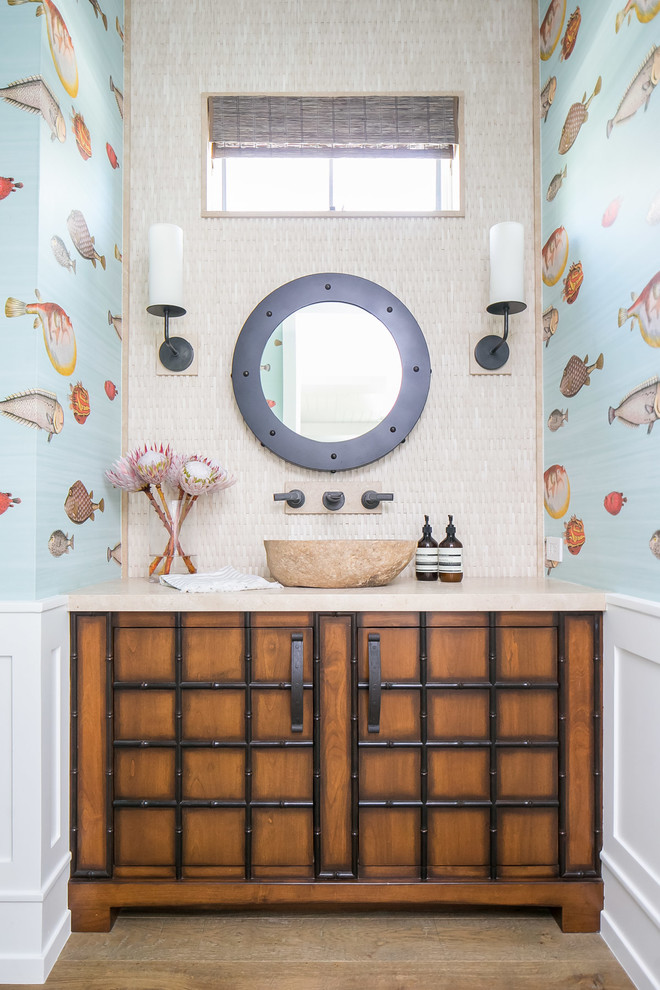 Inspiration for a mid-sized tropical powder room in Orange County with multi-coloured walls, medium hardwood floors, a vessel sink, brown floor, beige benchtops, furniture-like cabinets and medium wood cabinets.