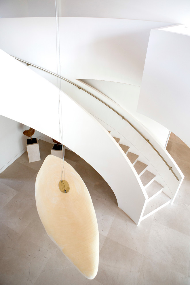 Пример оригинального дизайна: большая изогнутая лестница в современном стиле с ступенями из известняка и подступенками из известняка